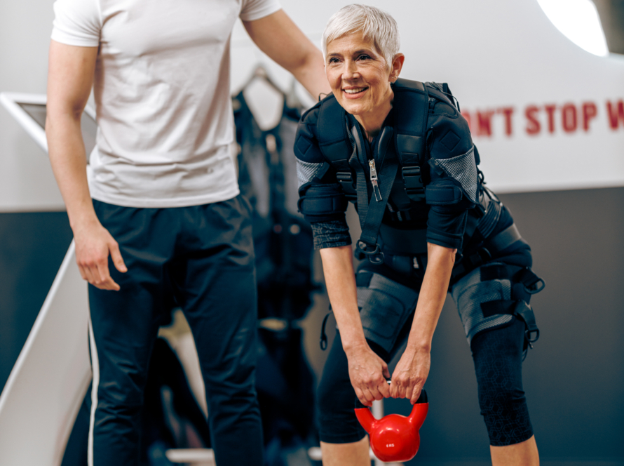 Senior Woman Doing EMS Workout With Coach In The Gym